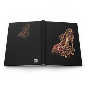 Peut inclure: Un carnet à couverture rigide noire présentant une grande illustration ornée d'un soulier à talon sur la couverture droite et une version plus petite sur la gauche. Le motif est orné de filigrane doré, de pierres rouges et de perles.