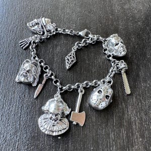 Puede incluir: Un brazalete de plata con dijes de personajes de pel&iacute;culas de terror, incluyendo Jason Voorhees, Freddy Krueger, Michael Myers y Pennywise. Los dijes est&aacute;n unidos a una cadena de plata con un cierre de langosta.