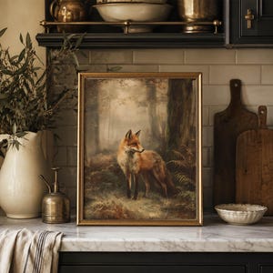 May include: A framed rectangular wall art print featuring a detailed painting of a red fox standing in a misty forest setting with trees and ferns. The artwork is enclosed in a thin gold-toned frame and displayed on a kitchen counter.