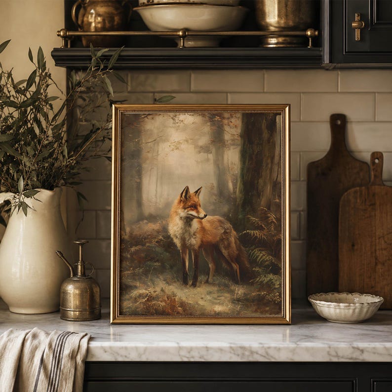 May include: A framed rectangular wall art print featuring a detailed painting of a red fox standing in a misty forest setting with trees and ferns. The artwork is enclosed in a thin gold-toned frame and displayed on a kitchen counter.