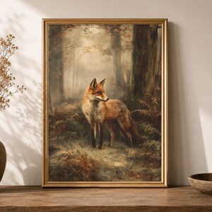 May include: A framed wall art print featuring a red fox standing in a misty, sunlit forest. The fox has orange and white fur and is positioned among dark tree trunks and green ferns. The artwork is enclosed in a thin, metallic gold frame.