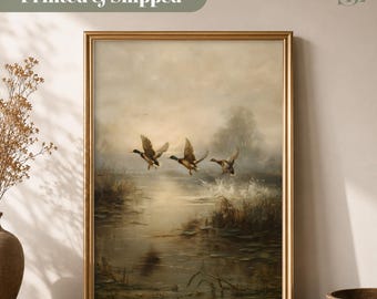 以下が含まれることがあります： 霧のかかった湿地帯の上を飛ぶ3羽のマガモを描いた油絵の額入りアートプリント。作品は細いゴールドのフレームに収められており、柔らかな光に包まれた穏やかな風景が表現されています。