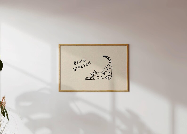 Puede incluir: Una impresi&oacute;n enmarcada con una ilustraci&oacute;n en blanco y negro de un gato estir&aacute;ndose, adornada con patrones en forma de coraz&oacute;n. Las palabras "BIG STRETCH" est&aacute;n escritas encima del gato. La obra de arte se presenta sobre un fondo neutro.