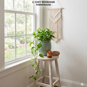 May include: A light green fluted ceramic planter containing a trailing green pothos plant, a small amber glass candle, and a wooden bowl on a distressed white wooden stool. A cream-colored macrame wall hanging is displayed above the stool.