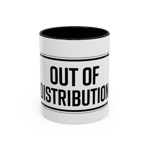 Könnte beinhalten: Weißer Keramikbecher mit schwarzem Innenraum. Der Becher trägt den Text "OUT OF DISTRIBUTION" in fetten schwarzen Buchstaben, zentriert auf der weißen Oberfläche, mit schwarzen Rändern.