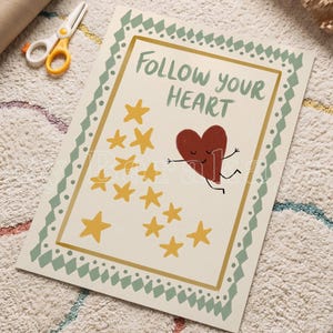 May include: A rectangular print on a cream background featuring the text FOLLOW YOUR HEART in green. A dark red heart character with a face and limbs is depicted next to a cluster of yellow stars. The print has a green geometric border.