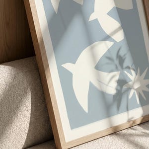 May include: A framed art print featuring a light blue background with white bird and star-like shapes. The frame is made of light-colored wood. The words "frame mockup" are at the top of the image.