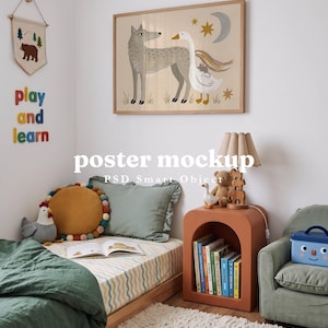 May include: A framed wall poster featuring a gray wolf and a white goose under a moon and stars, displayed above a bed with a green duvet, a round mustard pillow, a terracotta arched nightstand, and a blue toy box in a child's bedroom.