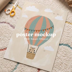 Op de afbeelding: Een rechthoekige poster-mockup met een illustratie van een heteluchtballon met een kat in de mand, tegen een beige lucht met witte wolken. De tekst "poster mockup" en "PSD Smart Object" staat in het wit in het midden gedrukt.