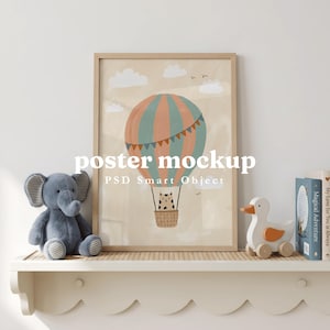 May include: A framed poster mockup featuring a hot air balloon illustration with a cat in the basket, set against a beige sky with clouds. The poster is displayed on a shelf alongside a gray plush elephant and a wooden duck toy.