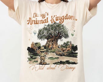 May include: Ivory-colored t-shirt featuring the text "Disney's Animal Kingdom" above an illustration of the Tree of Life and Mickey Mouse. The shirt also has the text "Wild about Disney" and the Comfort Colors logo.