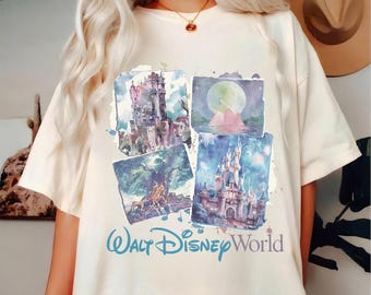 May include: Cream-colored t-shirt featuring a watercolor design of Disney World landmarks. The design includes images of a castle, a tower, and a moonlit scene, with the words "Walt Disney World" in blue script.