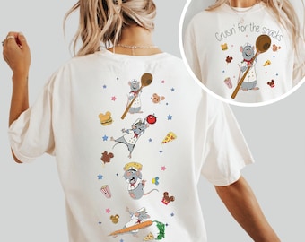 May include: Ivory-colored t-shirt featuring a cartoon chef rat with a wooden spoon, surrounded by food illustrations. The text "Cruisin' for the snacks" is printed on the front. The word "IVORY" is printed at the bottom.
