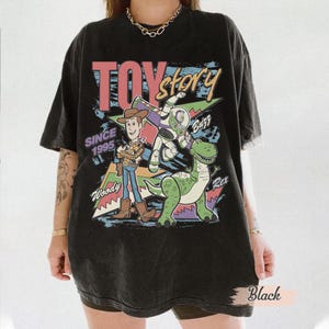 May include: Black t-shirt featuring a colorful graphic of Woody, Buzz Lightyear, and Rex from Toy Story. The design includes the text "TOY STORY" and "SINCE 1995". The shirt is a vintage style, with a slightly faded appearance.