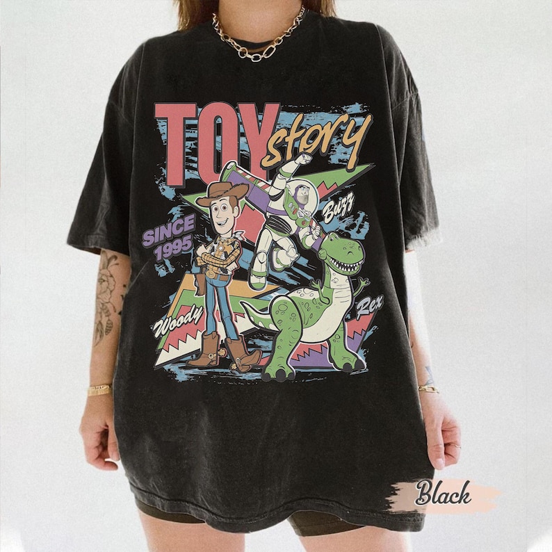 May include: Black t-shirt featuring a colorful graphic of Woody, Buzz Lightyear, and Rex from Toy Story. The design includes the text "TOY STORY" and "SINCE 1995". The shirt is a vintage style, with a slightly faded appearance.