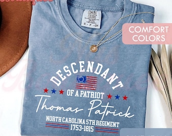 Op de afbeelding: Een jeansblauw t-shirt met een witte grafische print met de tekst Descendant of a Patriot, Thomas Patrick, North Carolina 5th Regiment, 1753-1815, voorzien van een kleine Amerikaanse vlag en rode en blauwe sterren. Het t-shirt heeft een Comfort Colors label.