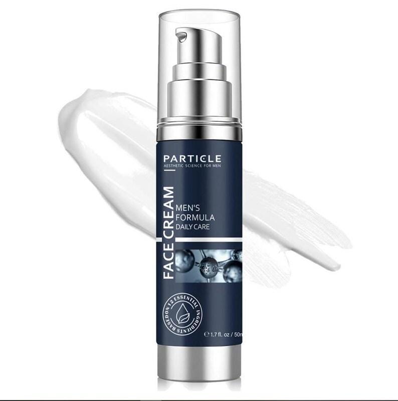 Puede incluir: Un frasco de crema facial plateado y azul marino con el texto "PARTICLE" y "MEN'S FORMULA DAILY CARE". El frasco contiene 50 ml de crema, con una mancha de crema blanca en el fondo.