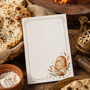 May include: A rectangular notepad with horizontal lines and a decorative border. The bottom right corner features a cartoon illustration of a smiling loaf of bread wearing a checkered apron, surrounded by wheat stalks and small green leaves.