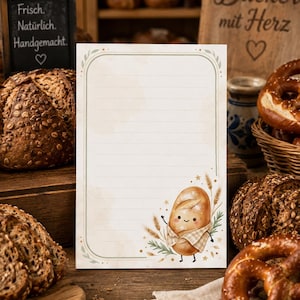 May include: A rectangular piece of stationery paper featuring horizontal lines and a rounded green border. The bottom right corner displays a cartoon illustration of a smiling loaf of bread wearing a checkered scarf, surrounded by wheat stalks.