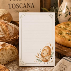 May include: A rectangular notepad with horizontal lines and a decorative border featuring a cute cartoon bread character wearing a checkered apron, surrounded by wheat stalks and green leaves, set against a light cream background.