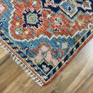 K&ouml;nnte beinhalten: Nahaufnahme einer Ecke eines gemusterten Teppichs mit traditionellem Design. Der Teppich weist eine Kombination aus Farben auf, darunter Rost, Blau und Creme. Die Kanten sind mit Fransen versehen.