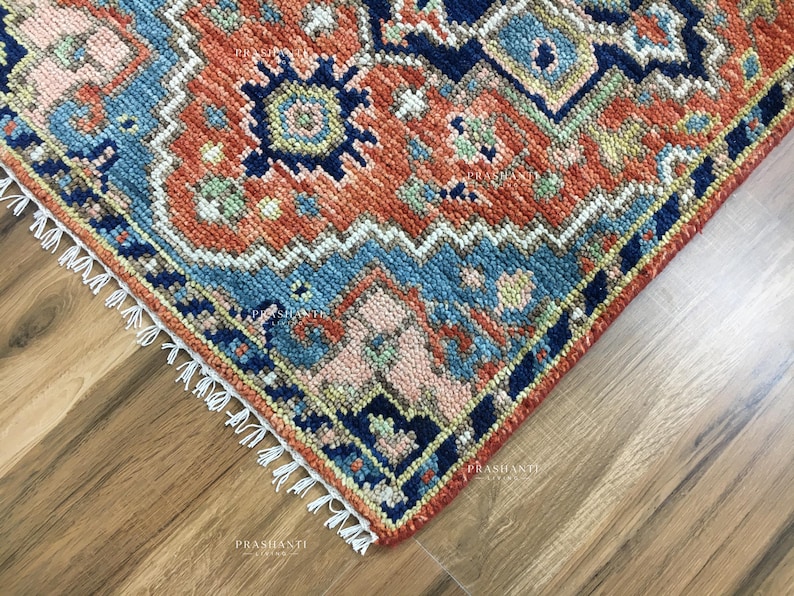 K&ouml;nnte beinhalten: Nahaufnahme einer Ecke eines gemusterten Teppichs mit traditionellem Design. Der Teppich weist eine Kombination aus Farben auf, darunter Rost, Blau und Creme. Die Kanten sind mit Fransen versehen.