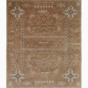 May include: A rectangular area rug in a warm brown tone featuring a symmetrical pattern of floral motifs in the corners, geometric borders, and central diamond shapes. The rug displays the text PRASHANTI LIVING printed multiple times across the surface.