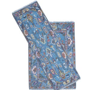 May include: A rectangular area rug featuring a vibrant blue base colour with intricate, multi-coloured floral and geometric patterns in shades of orange, pink, white, and dark blue. The rug has a fringed edge and a detailed border design.