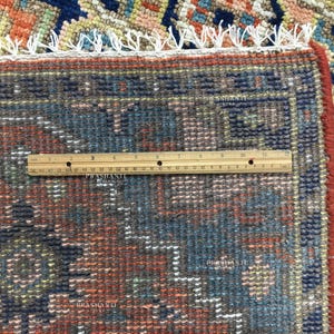 K&ouml;nnte beinhalten: Nahaufnahme eines Teils eines gemusterten Teppichs mit einem Lineal. Der Teppich weist eine Mischung aus Farben auf, darunter Blau, Orange und Rot, mit einem detaillierten geometrischen Design. Das Lineal misst in Zentimetern.