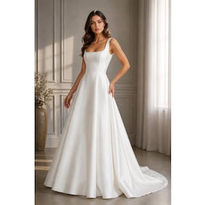 May include: A floor-length white gown featuring a square neckline, thick shoulder straps, and a fitted bodice that transitions into a full, flowing A-line skirt with a subtle train. The garment is crafted from a smooth, solid white fabric.