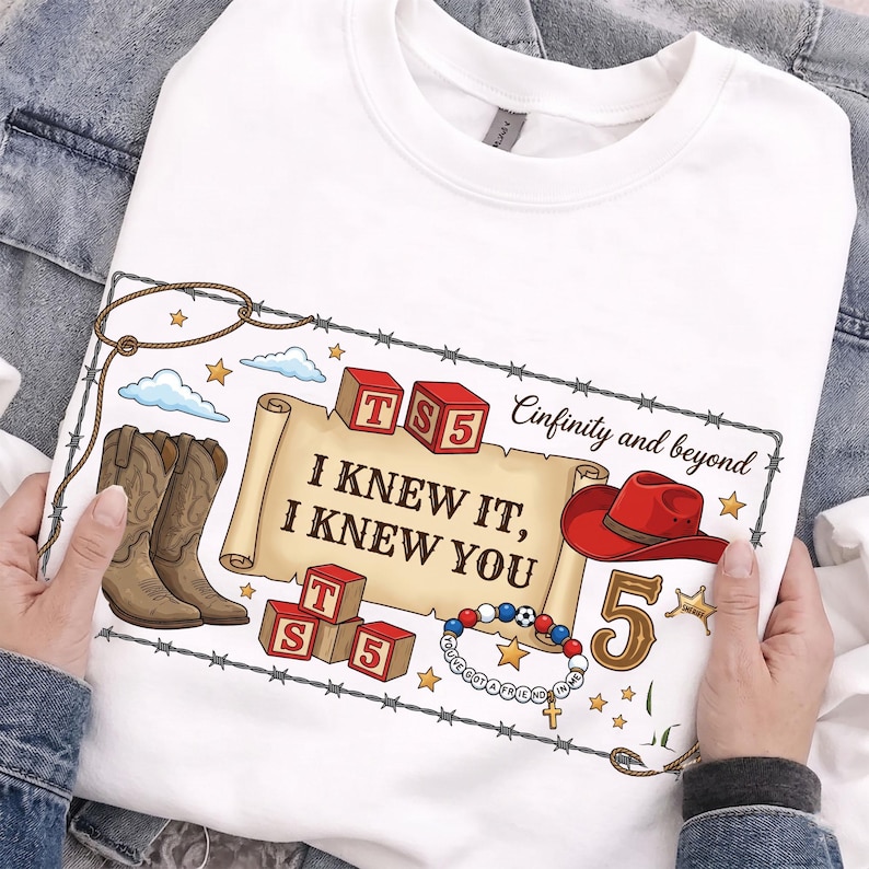 Pu&ograve; includere: Una t-shirt bianca con una stampa grafica bordata da filo spinato, stivali da cowboy marroni, un cappello da cowboy rosso, blocchi dell'alfabeto con le lettere T, S e 5, una pergamena con il testo I KNEW IT, I KNEW YOU e Cinfinity and beyond.