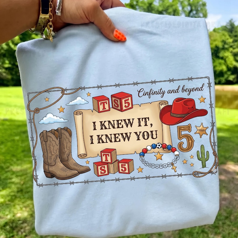 Pu&ograve; includere: Una t-shirt azzurro chiaro con una stampa grafica raffigurante una pergamena con il testo "I KNEW IT, I KNEW YOU", blocchi "TS5", un cappello da cowboy rosso, stivali marroni, un braccialetto di perline, un cactus, una stella e "Cinfinity and beyond".