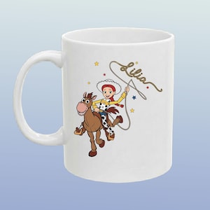 May include: A white ceramic mug featuring a colourful illustration of a cowgirl character with red hair riding a brown horse. The character is holding a lasso, and the name Lilia is written in cursive script above the lasso. Small yellow and blue stars surround the figures.