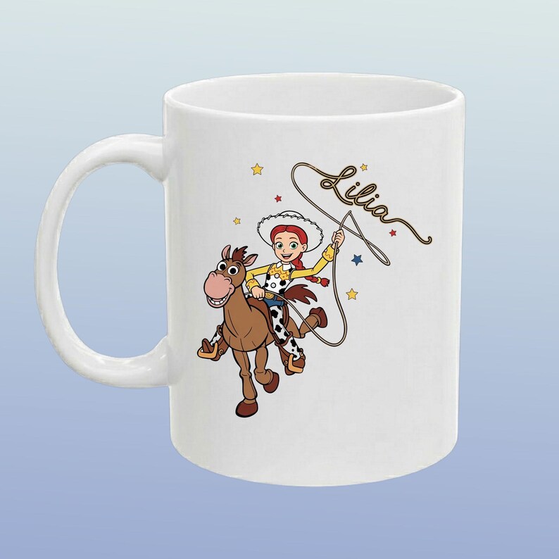 May include: A white ceramic mug featuring a colourful illustration of a cowgirl character with red hair riding a brown horse. The character is holding a lasso, and the name Lilia is written in cursive script above the lasso. Small yellow and blue stars surround the figures.