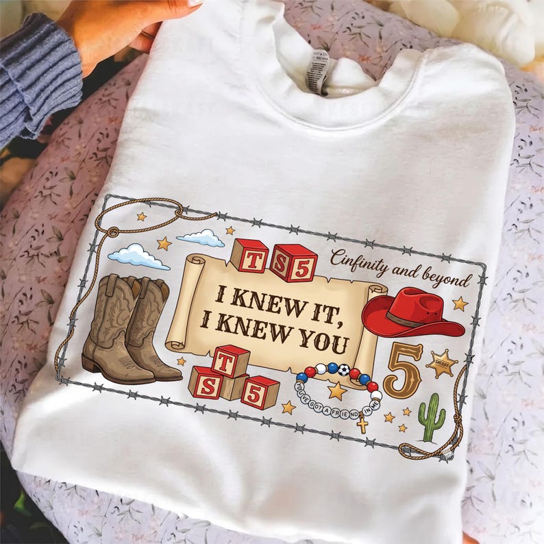 Pu&ograve; includere: Una t-shirt bianca con una stampa grafica di una pergamena con il testo "I KNEW IT, I KNEW YOU", circondata da stivali da cowboy, blocchi rossi "TS 5", un cappello da cowboy rosso, un numero 5, un cactus e un braccialetto di perline.