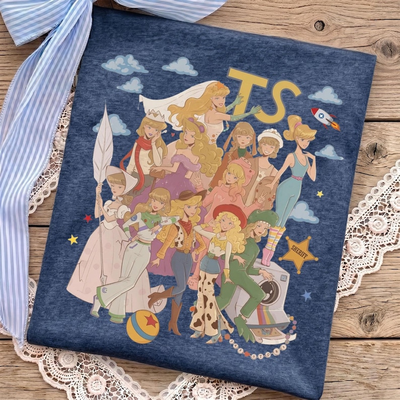May include: A dark blue heathered t-shirt featuring a graphic print of multiple illustrated characters in various outfits, including a space ranger suit and cowgirl attire, with the letters TS, a rocket ship, a ball, and a sheriff star badge.