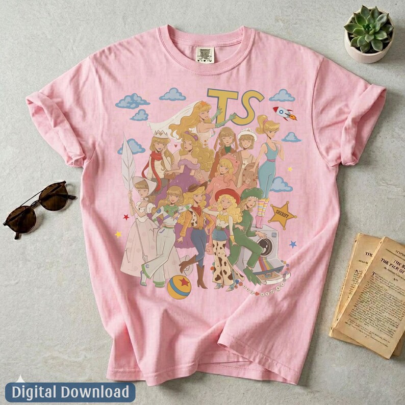 May include: A light pink t-shirt featuring a graphic print of various animated characters in a collage style. The design includes the letters TS, a rocket, a star, and a ball. The shirt has short sleeves and a crew neckline, showcasing a colorful illustration.