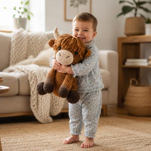 May include: A brown and tan crocheted highland cow plush toy with dark brown hooves, a cream-colored muzzle, and small horns. The toy features a textured yarn construction with a shaggy mane and round black eyes, held in a standing position.