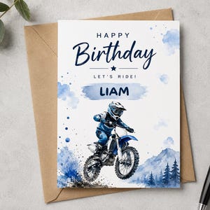 Könnte beinhalten: Eine rechteckige Geburtstagskarte mit einer Aquarellillustration eines Motocross-Fahrers auf einem blauen Dirtbike. Der Text lautet HAPPY Birthday LET'S RIDE! LIAM. Das Design enthält blaue Aquarellspritzer, Berge und Tannenbäume.