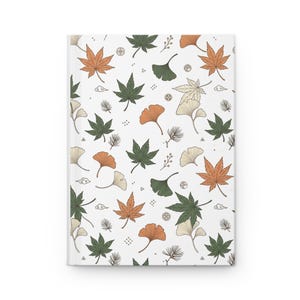May include: A hardcover notebook with a white cover featuring a repeating pattern of orange and dark green maple leaves, ginkgo leaves, pine needles, small berries, and stylized cloud icons arranged across the entire surface of the front cover.