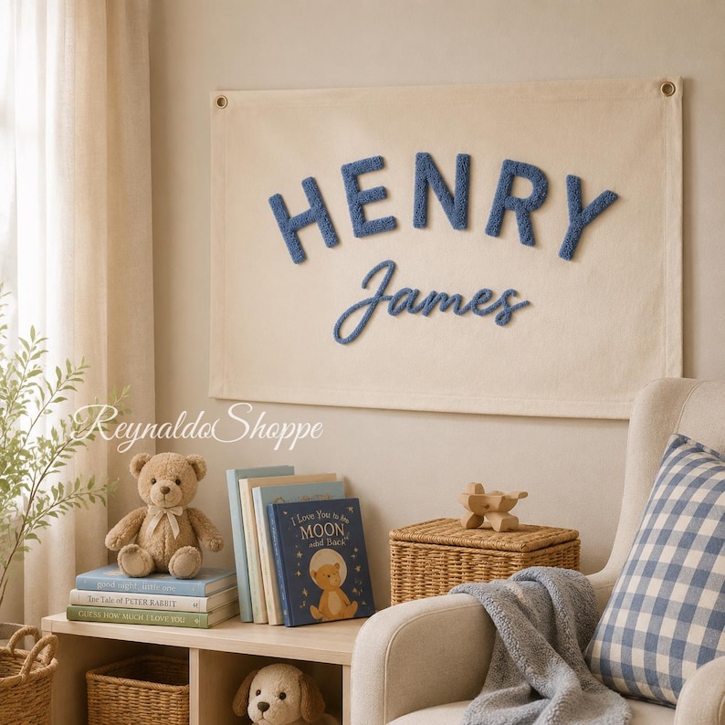 May include: A rectangular cream-colored fabric wall hanging featuring the name HENRY JAMES in raised, textured blue lettering. The word HENRY is in a bold, block-style font, while the name James is in a cursive, script-style font.