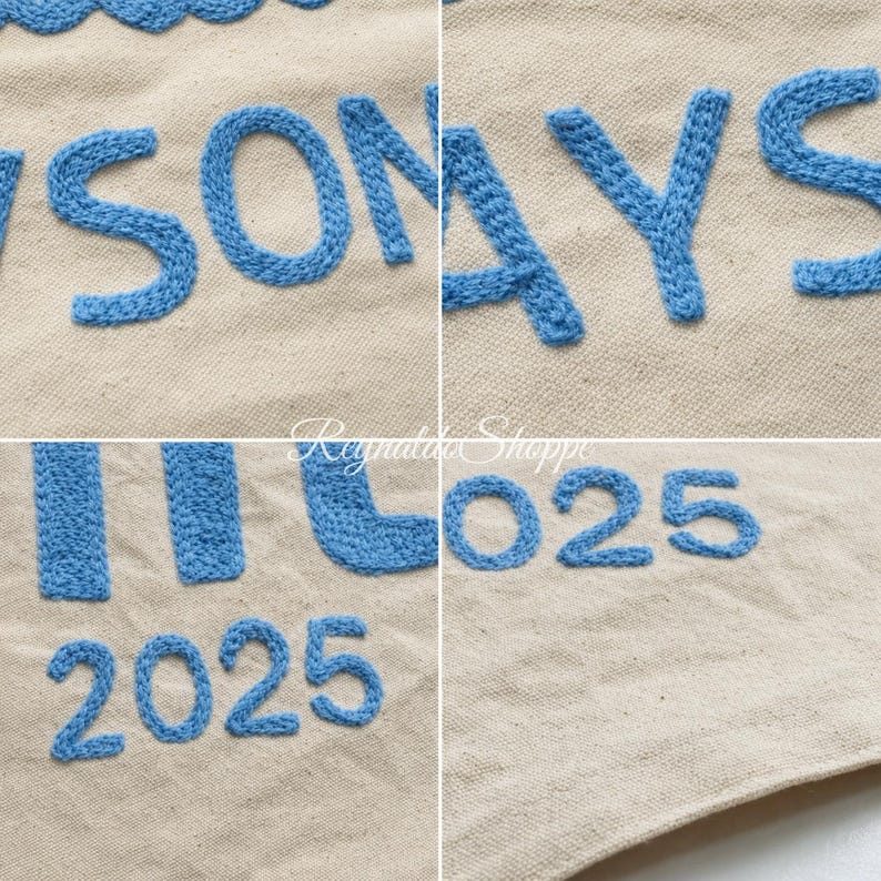 May include: A beige fabric surface featuring blue embroidered lettering and numbers. The visible text includes parts of words and the number 2025. The embroidery has a raised, textured appearance against the plain, light-colored woven textile background.