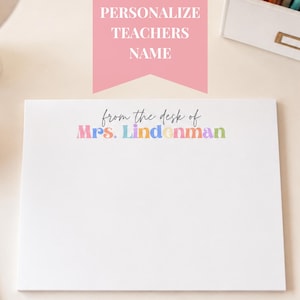 May include: A white rectangular notepad featuring the black cursive text from the desk of followed by the name Mrs. Lindenman printed in a multi-coloured, bold, rounded font. The notepad is blank below the text, providing space for writing notes.