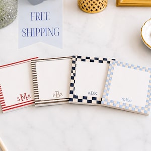 May include: Four square paper notepads with white centers and patterned borders. The first has red stripes and the monogram SMR, the second has brown stripes and pBs, the third has a navy checkerboard and aDk, and the fourth has light blue checks and mKc.