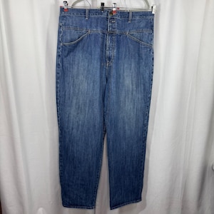 May include: High-waisted blue denim jeans featuring a button-front closure, belt loops, and two front pockets with angled seams. The medium-wash fabric displays subtle fading throughout the legs, providing a consistent texture and straight-leg cut.