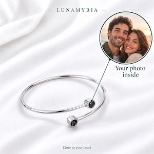 May include: A silver-toned open cuff bracelet featuring two circular ends. A circular inset shows a photograph of a smiling couple. The text LUNAMYRIA appears at the top, with the text Your photo inside and Close to your heart below.