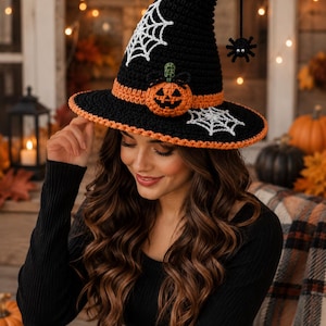 May include: A black crocheted witch hat featuring an orange band, a small orange pumpkin appliqué, white spiderweb embroidery on the crown and brim, and a dangling black spider ornament hanging from the pointed tip of the hat.