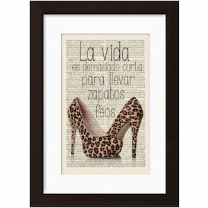 May include: A framed print with a quote in Spanish that reads "La vida es demasiado corta para llevar zapatos feos" which translates to "Life is too short to wear ugly shoes". The quote is printed on a vintage book page background with two leopard print high-heeled shoes.