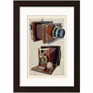 Puede incluir: Dos cámaras vintage con cuerpos de madera y fuelle se muestran en una página de un libro. Las cámaras son marrones y negras con detalles en latón. La página del libro está llena de texto en francés.