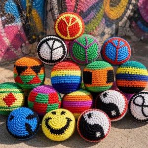 Puede incluir: Una colección de coloridos sacos de hacky tejidos a ganchillo. Cada pelota presenta diseños únicos, incluyendo símbolos de la paz, caras sonrientes y patrones geométricos. Las pelotas son de varios colores, como rojo, azul, verde y amarillo.